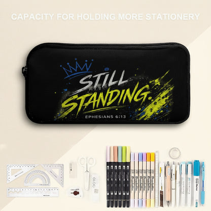 A black zippered pencil case with a graphic that reads 'STILL STANDING. EPHESIANS 6:13' in white and neon yellow, shown with stationery items including markers, pens, scissors, a ruler, and tape on a split white and pale blue background.