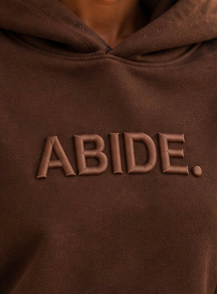 Brown ABIDE hoodie close-up of embossed front logo