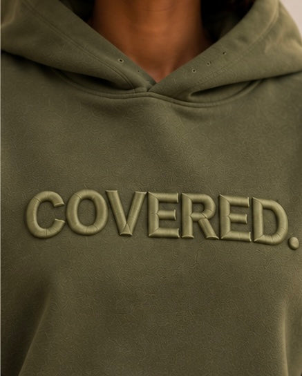 Close-up of army green hoodie with raised COVERED. logo on the chest