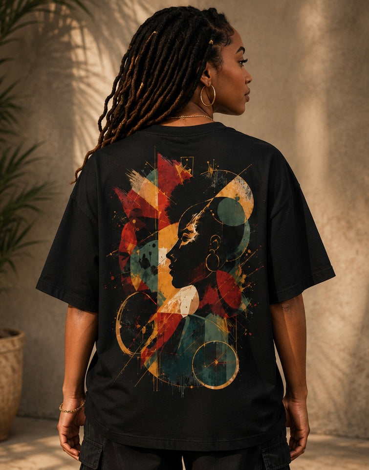 A woman viewed from behind wearing a black oversized T-shirt with a large abstract graphic print on the back. The design features a profile silhouette in dark blue and red, overlaid with geometric shapes in beige, gold, and teal.