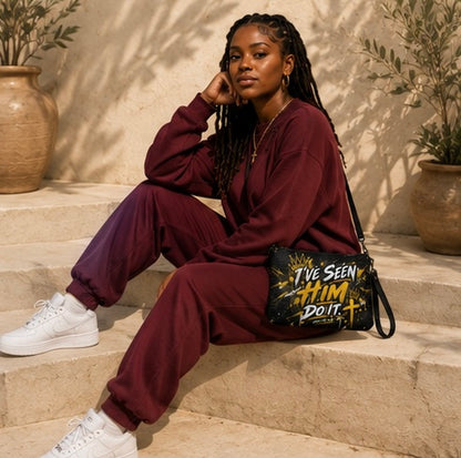A woman sits on stone steps wearing a matching burgundy sweatshirt and jogger pants set, white sneakers, and a black crossbody bag with yellow and white text that reads 'I've Seen HIM Do It'.
