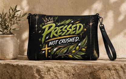 Black zippered crossbody bag on ledge with 'PRESSED NOT CRUSHED' logo and wrist strap