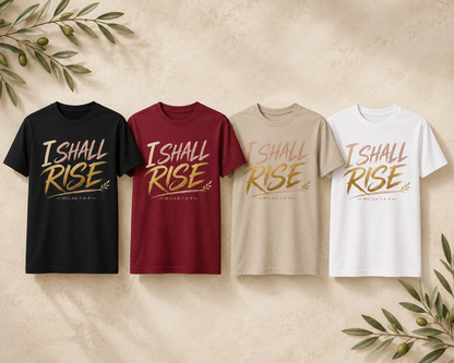 Four graphic T-shirts in black, burgundy, beige, and white, arranged side by side on a textured beige background with decorative olive branches in the corners. Each shirt features the words 'I SHALL RISE' in a metallic gold font with a small olive branch graphic and 'MERCED TO GOD' underneath.