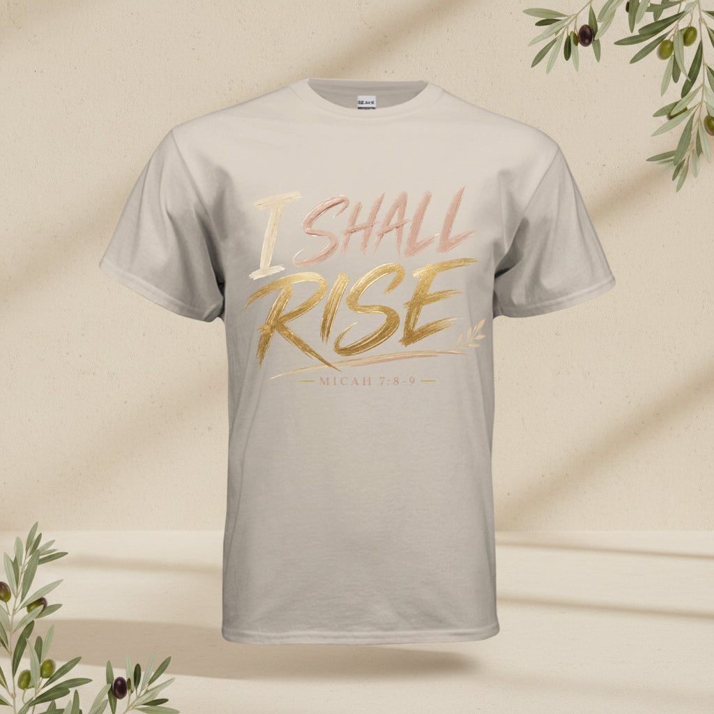 A light beige crewneck t-shirt featuring the text 'I SHALL RISE' in a metallic gold and rose gold gradient across the chest, with 'MICAH 7:9' printed below in a smaller gold font.