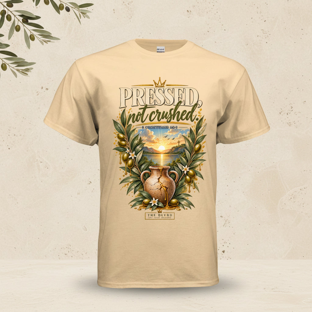A beige crewneck t-shirt featuring a graphic print on the front with the text 'PRESSED not crushed' and an illustration of an ancient clay pot surrounded by olive branches and a sunset landscape.