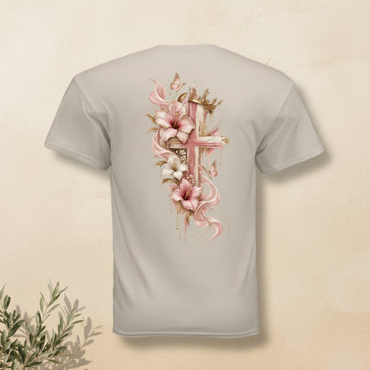 A light beige crewneck t-shirt shown from the back, featuring a large graphic print of a pink cross decorated with pink lilies, white flowers, and gold accents.