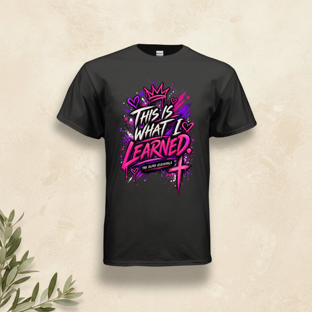 A black short-sleeve t-shirt with a vibrant graphic on the front that reads 'THIS IS WHAT I LEARNED' in stylized white and pink lettering, decorated with a crown, hearts, and a cross, on a plain white background.