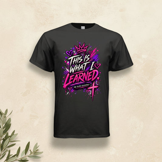 A black short-sleeve t-shirt with a vibrant graphic on the front that reads 'THIS IS WHAT I LEARNED' in stylized white and pink lettering, decorated with a crown, hearts, and a cross, on a plain white background.