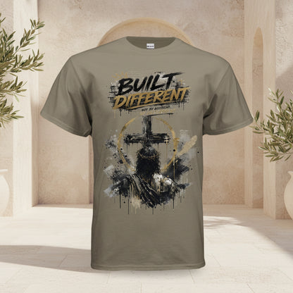 A taupe brown short-sleeve t-shirt with a distressed graphic on the front featuring a cross, a praying man, and the text 'BUILT DIFFERENT' in black and gold.